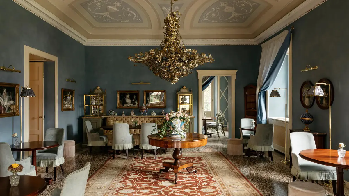 A drawing room with teal walls, gold furnishings, chandelier, and patterned rug
