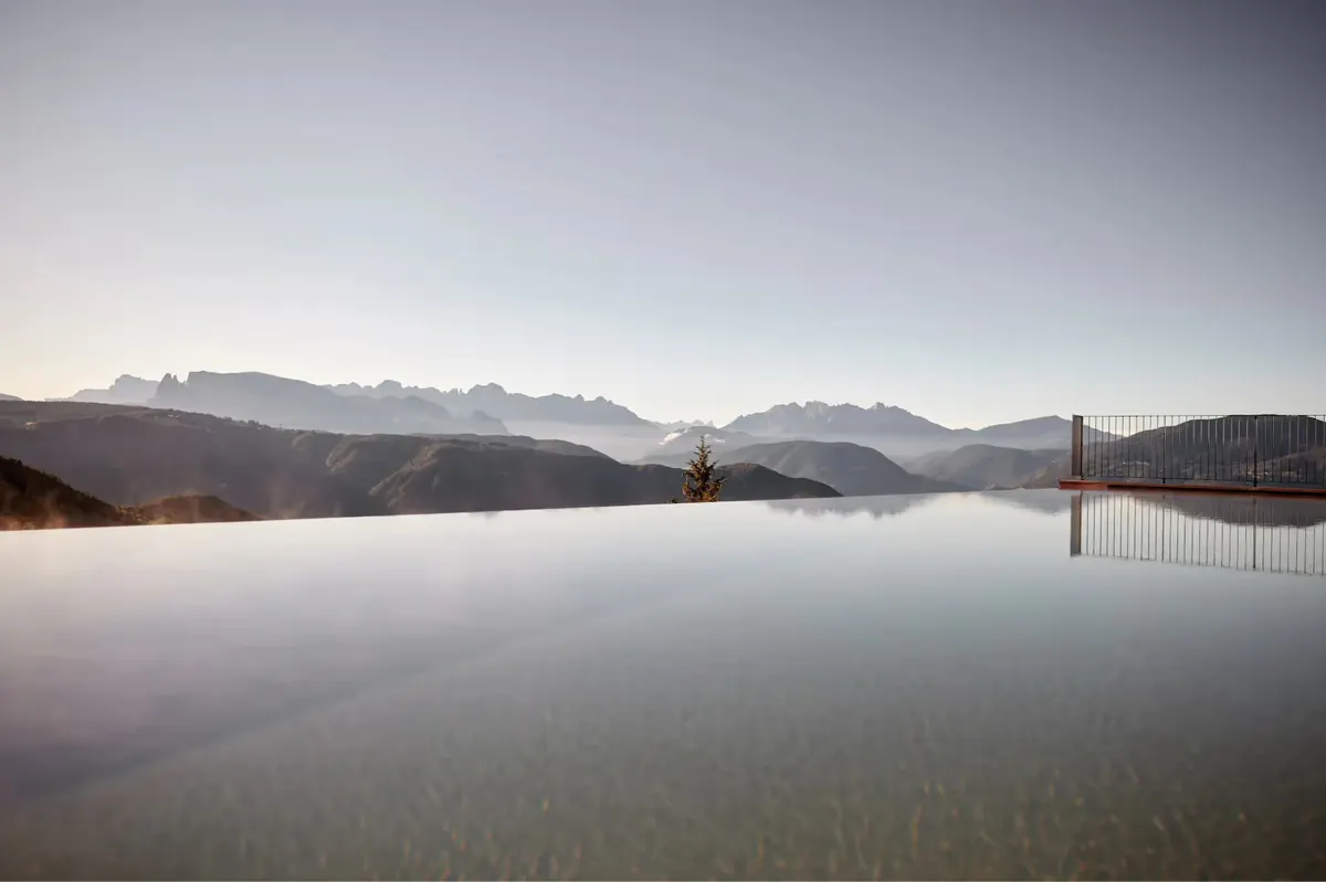 Reflection pool at sunrise with distant mountains and sparse trees in soft golden light