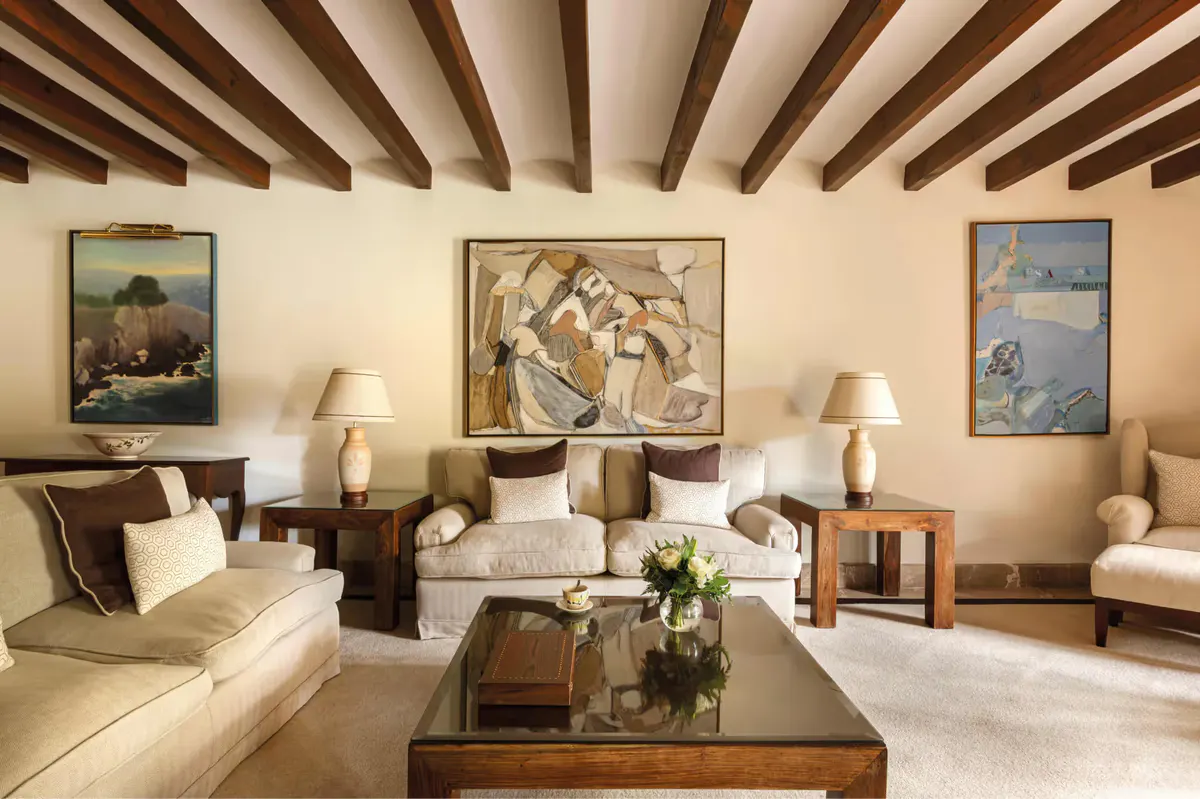 Formal sitting area with beamed ceiling, cream-toned furnishings, framed artwork, and arched doorway