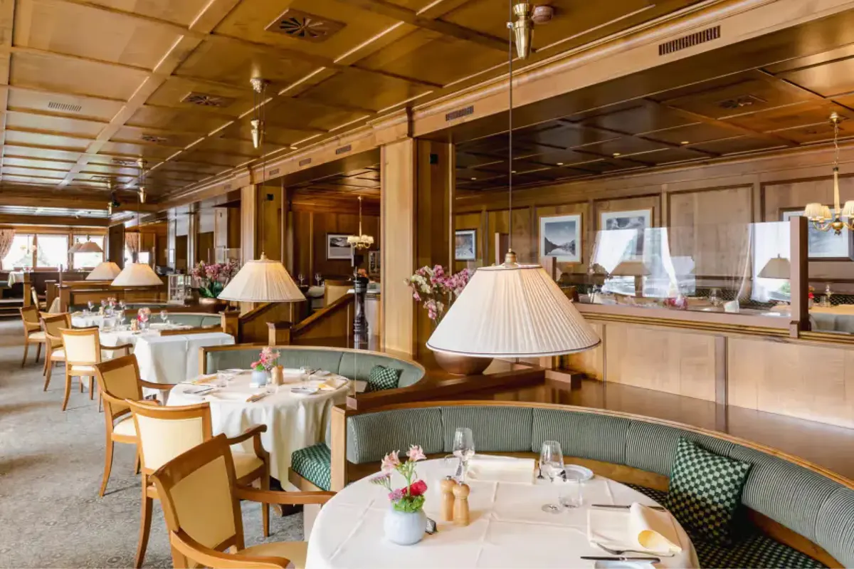 A restaurant with wood walls, table lamps, white-clothed settings, and warm ambient lighting