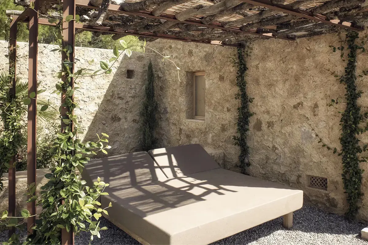 Sheltered outdoor sitting area beneath timber pergola with stone walls and natural vegetation