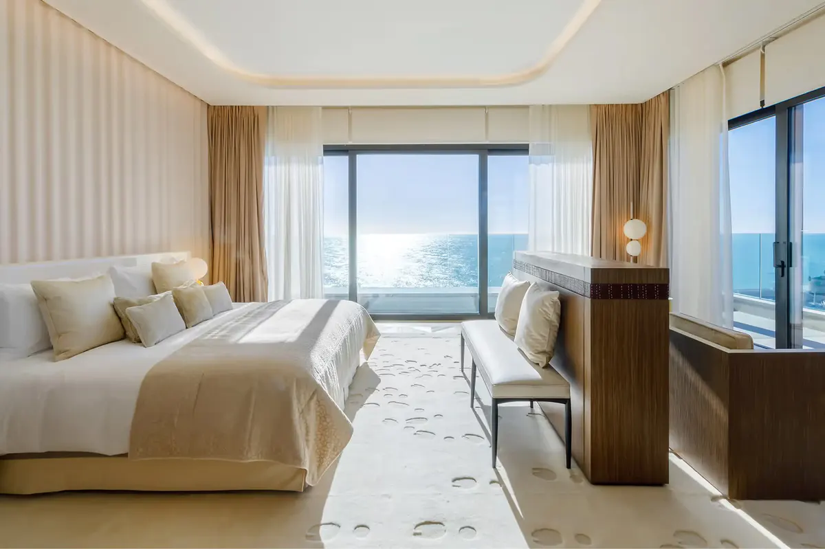 Bedroom with white bedding, beige striped walls, open doors to sea view balcony