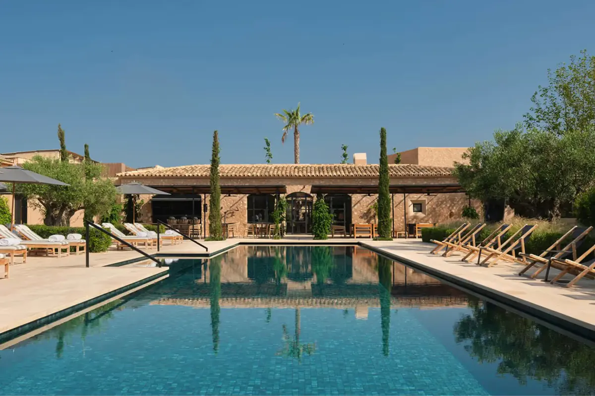 Outdoor pool surrounded by lounge chairs and terracotta mansion facade under blue sky