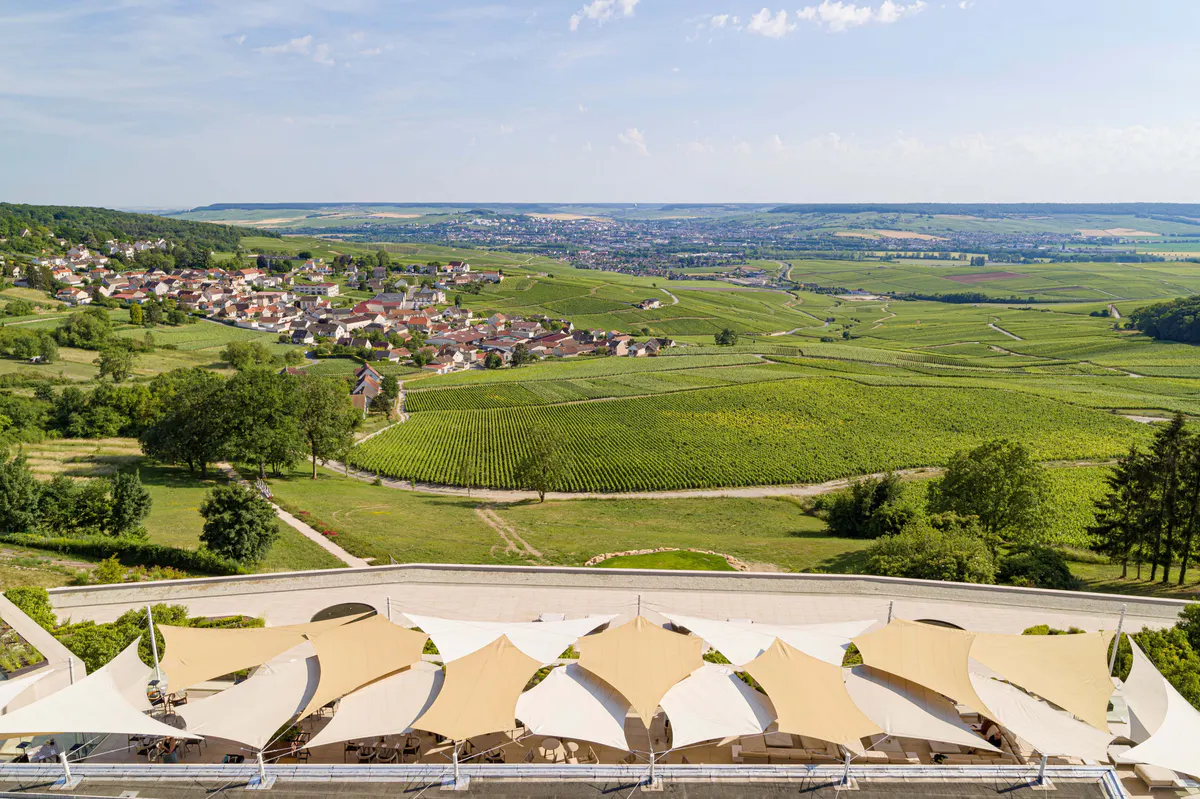 Expansive vineyard landscape with sunlit fields, villages, and hotel terrace in foreground