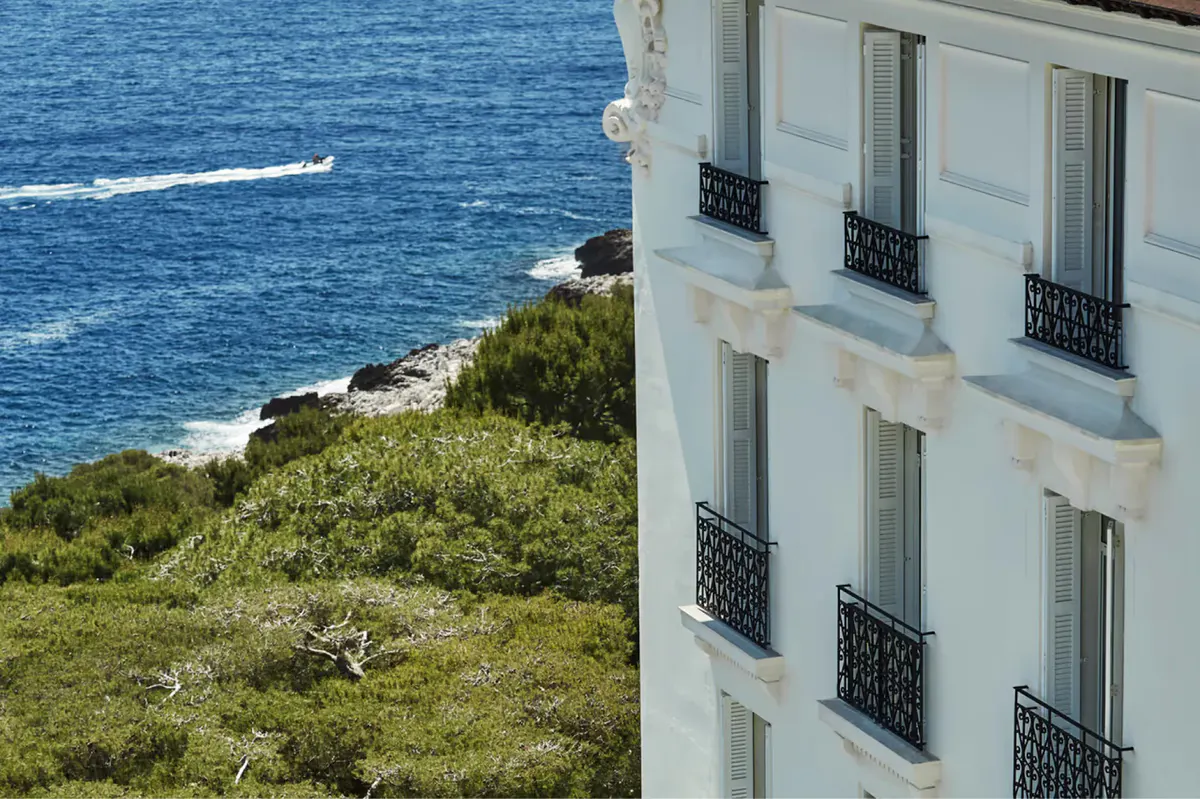 Cream facade with wrought-iron balconies above rocky coastline