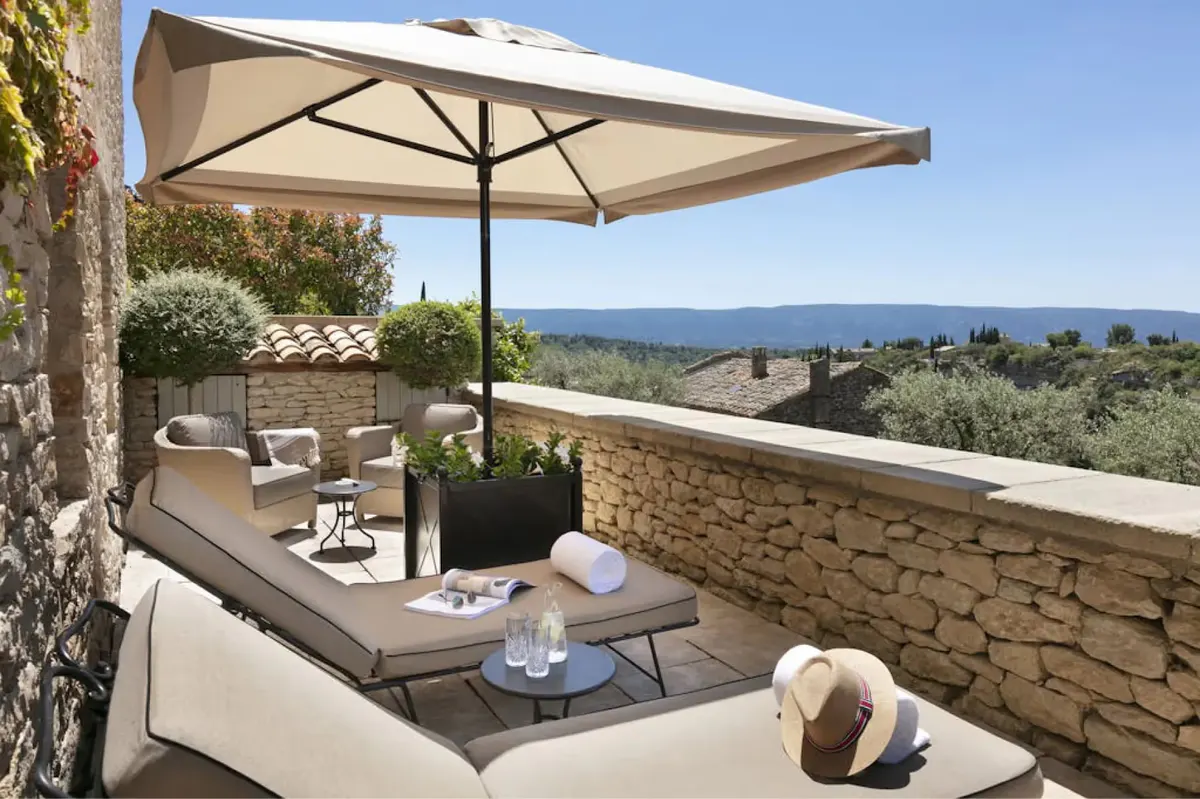 Shaded terrace with loungers and stone wall overlooking olive groves and distant mountains