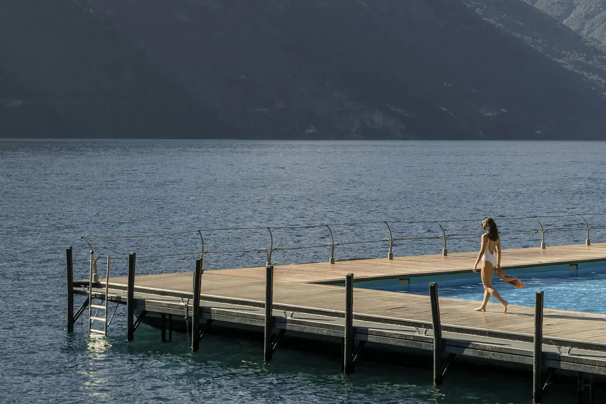 Woman walking on wooden platform pool deck over sparkling blue water