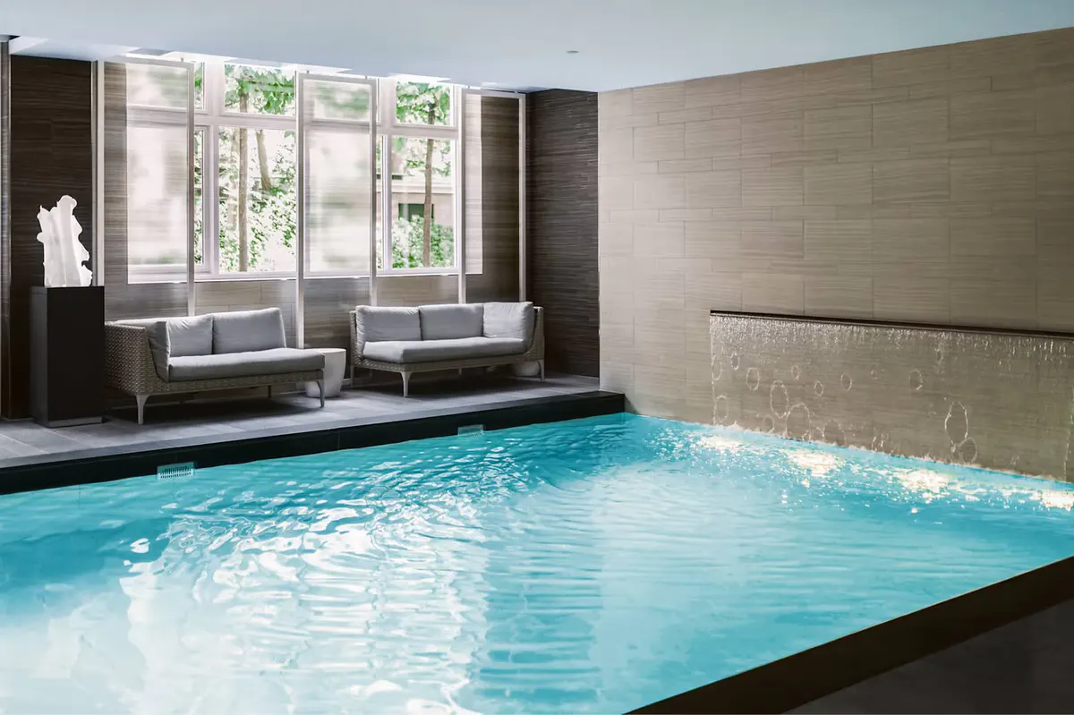 An indoor pool with rippling turquoise water next to relaxation seating and beige architectural columns