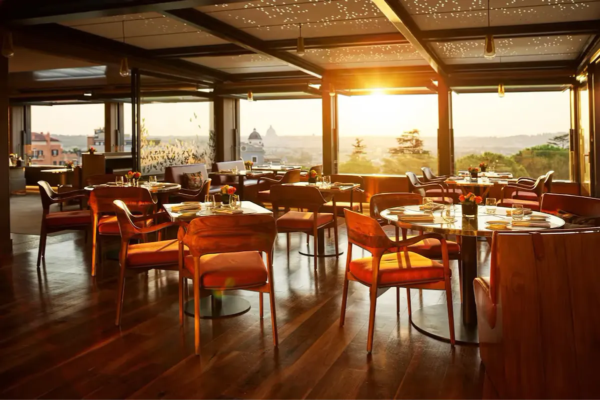 Il Giardino restaurant with wooden beams, orange leather chairs, and panoramic windows at sunset