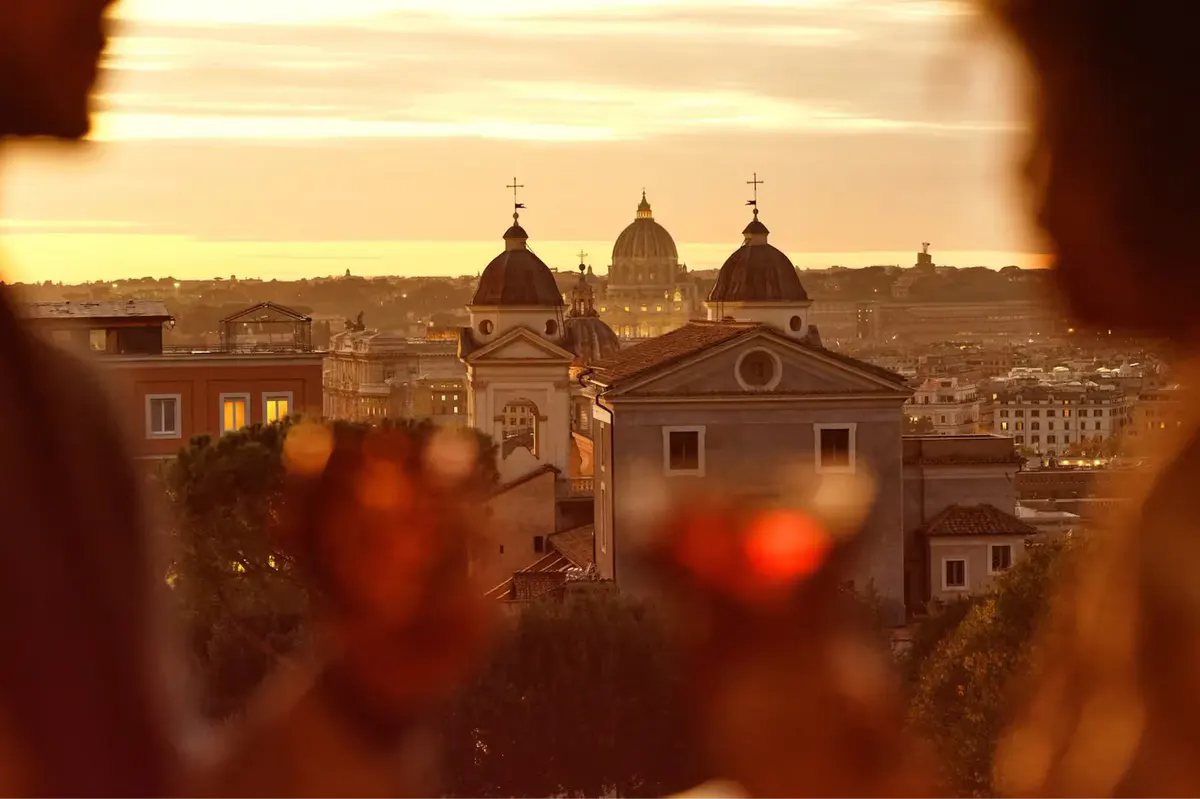 A view through ornate red glass vessels to Rome’s domes and architecture at golden hour
