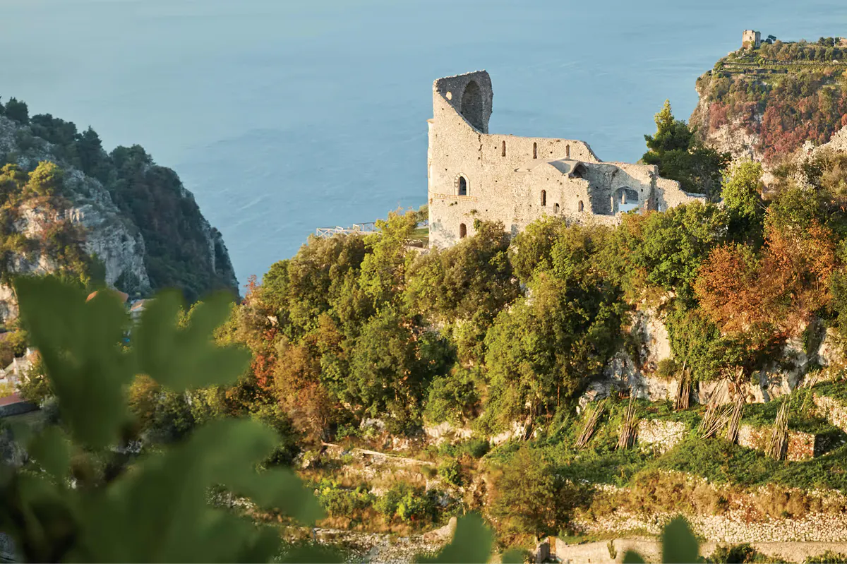 Medieval hilltop tower ruins surrounded by vegetation with sea and landscape beyond
