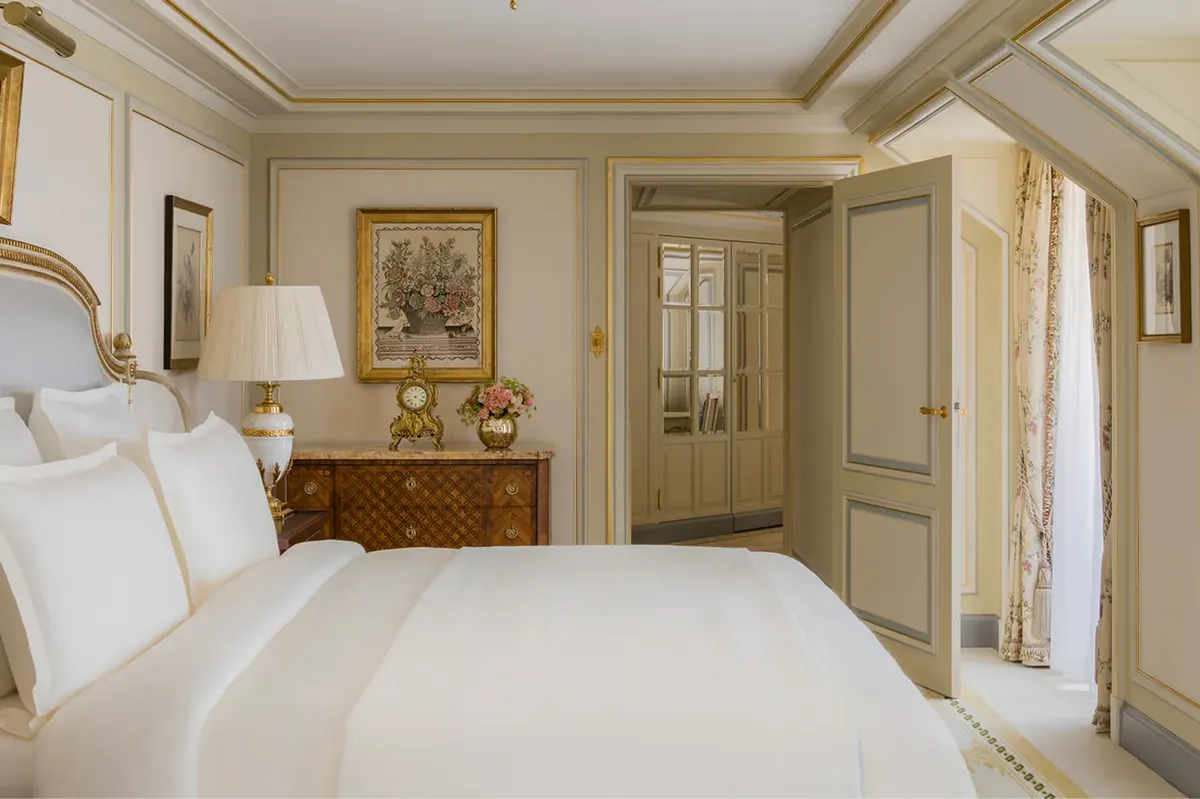 A bedroom with parquet floors, framed artwork, gilt accents, and cream color palette