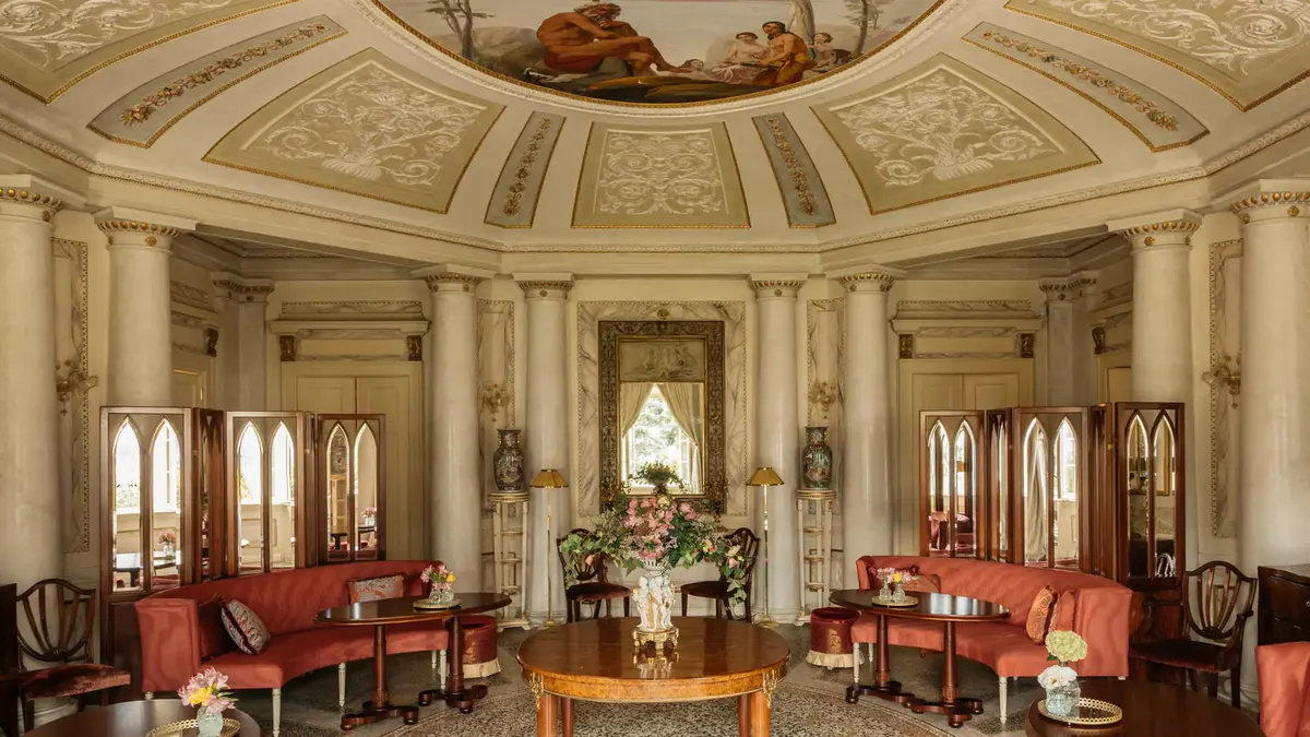 A cream-colored neoclassical salon with ornate ceiling, red velvet seating, and tall mirrors
