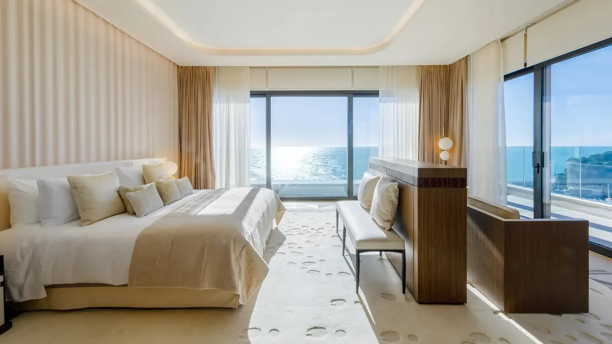 Bedroom with white bedding, beige striped walls, open doors to sea view balcony