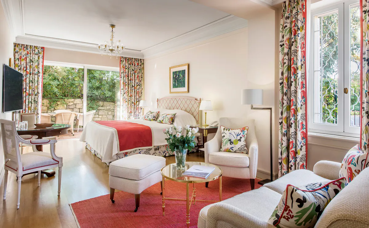 A guest room with red upholstered furniture, white walls, coral drapery, and traditional furnishings