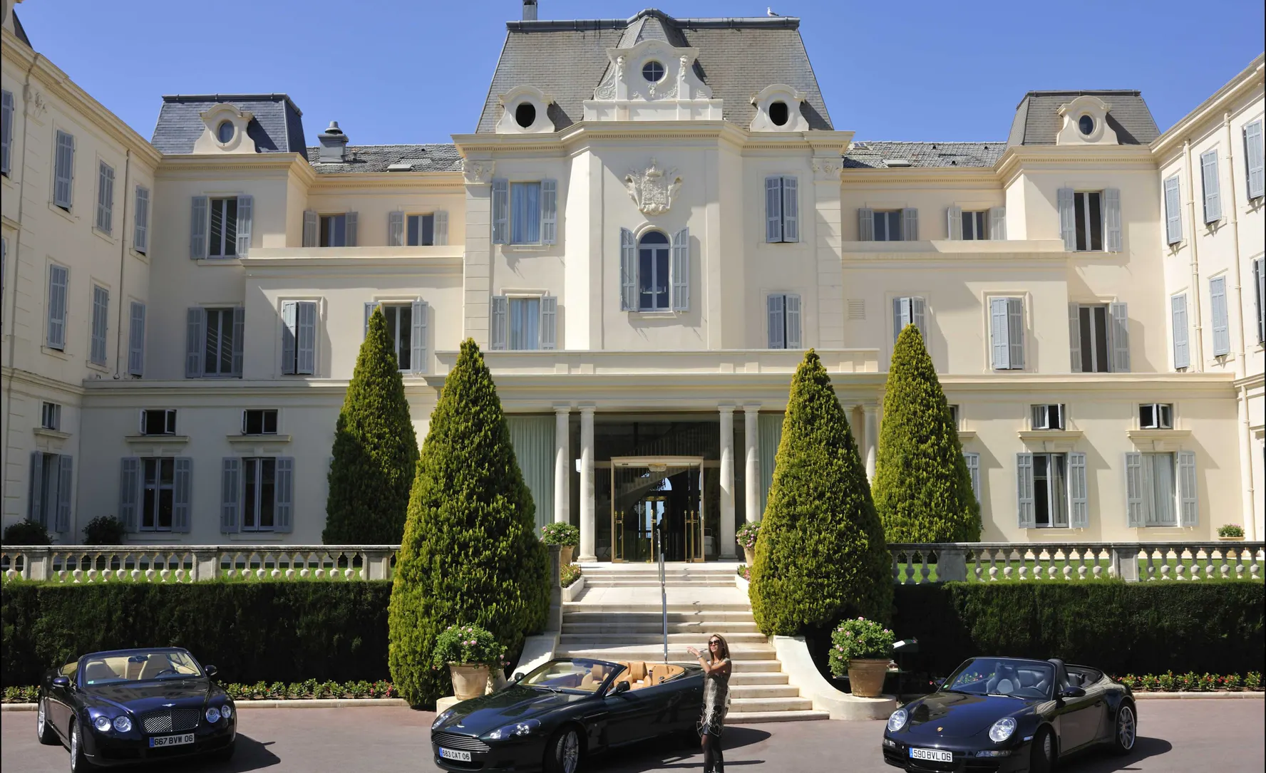 The façade of the Hôtel du Cap-Eden-Roc with clipped cypresses and cars on the drive