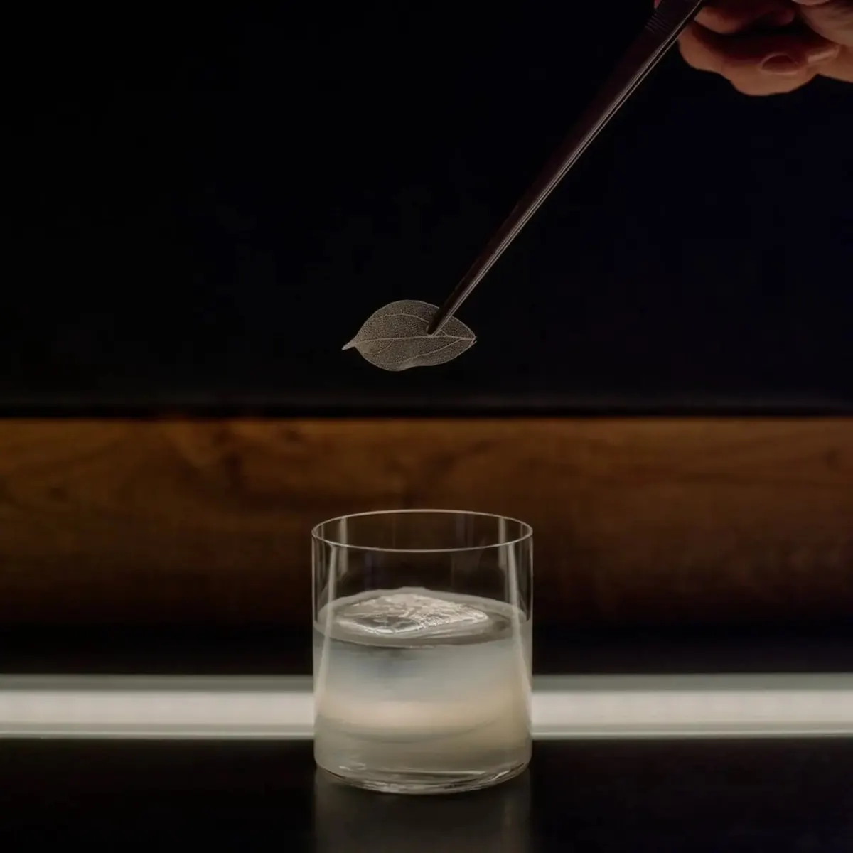 Cocktail garnished with a dried leaf, poured tableside over ice in a low rocks glass