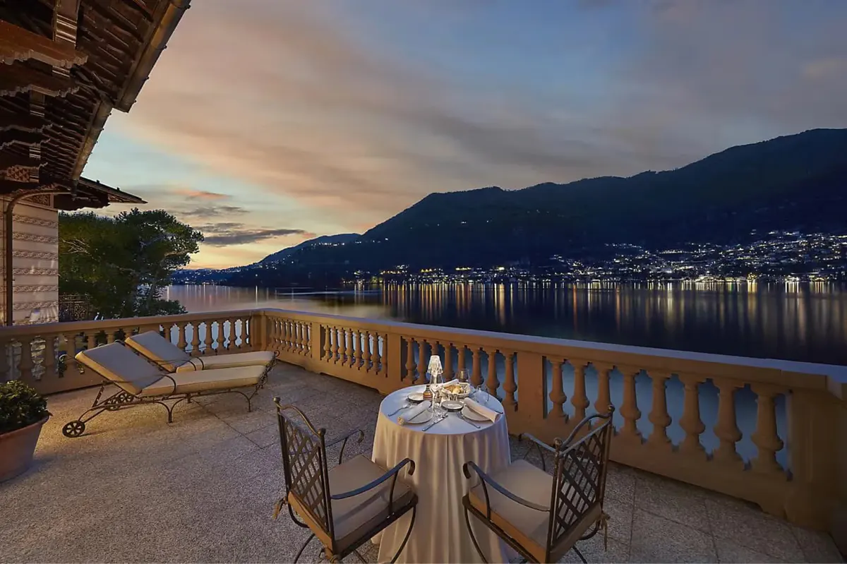Waterfront terrace at sunset with white furniture and distant mountains reflected in still water