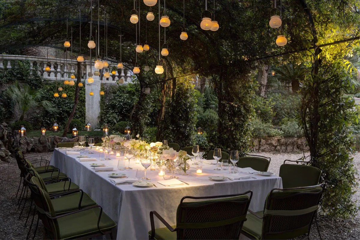 Outdoor table under hanging pendant lights with ivy and lush surroundings at night
