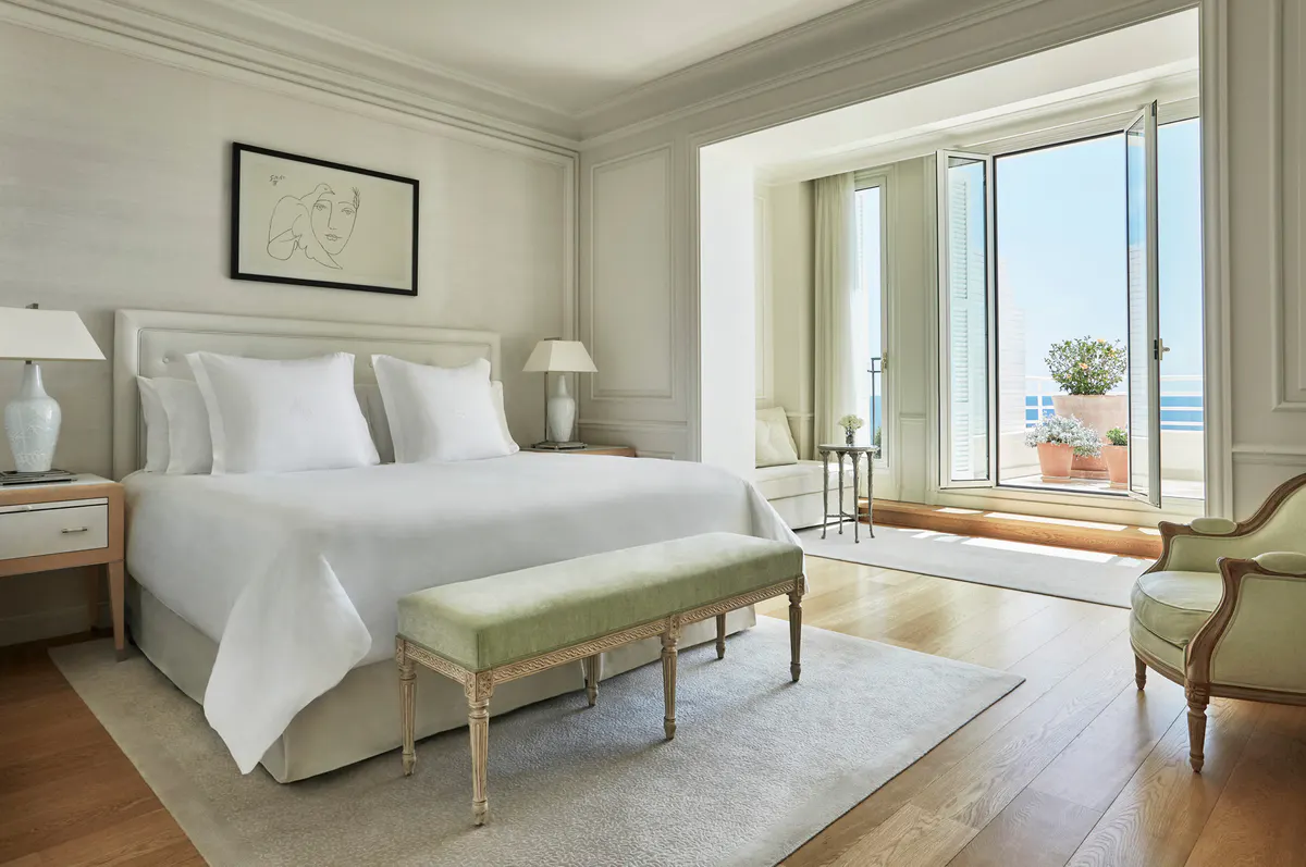 Bright bedroom with white linens, floor-to-ceiling doors opening to a sea-view terrace