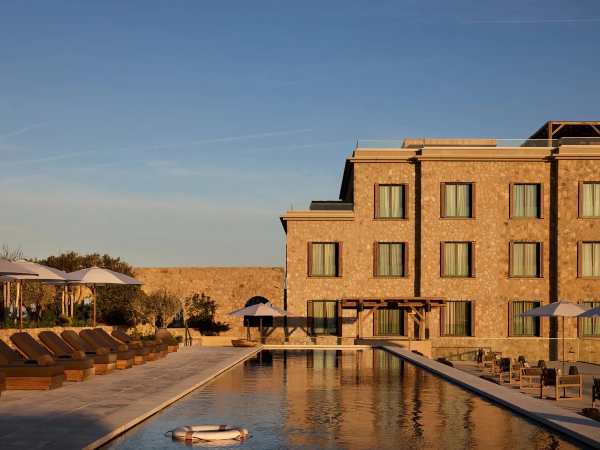 Morning light warms the stone hotel wing above a reflecting pool lined with white parasols