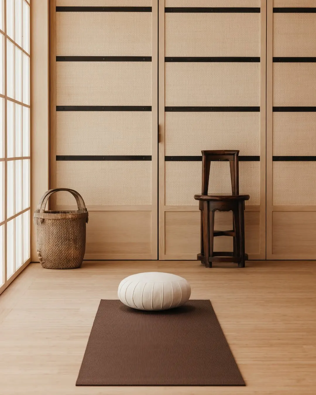 Yoga studio corner with a woven basket, wooden stool, and a meditation cushion on a floor mat