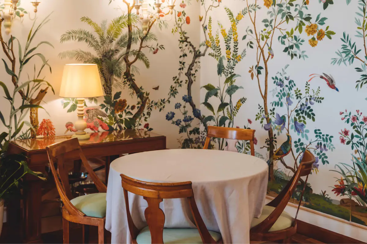 An intimate dining room with wallpapered walls, potted plants, and round table