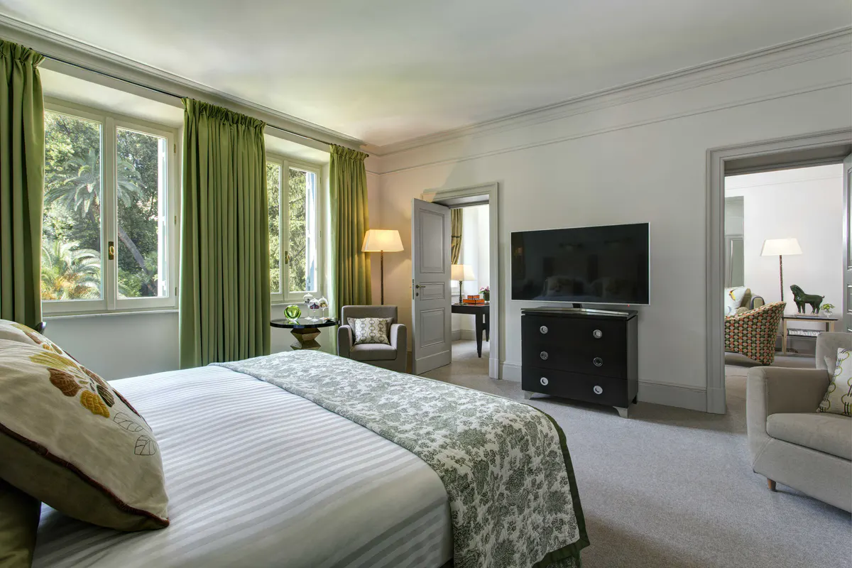 Bedroom with green curtains, white bedding, and garden views from multiple windows