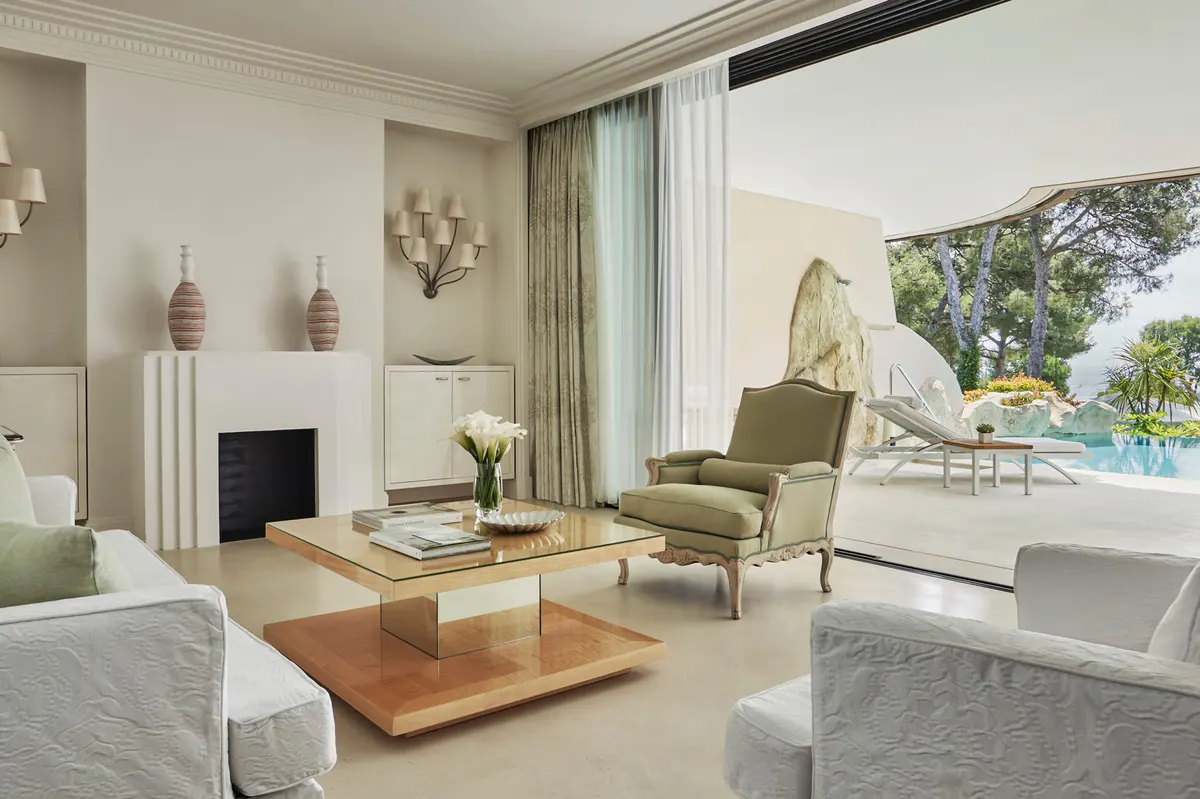 Suite with fireplace, pale furniture, and terrace overlooking pool and grounds