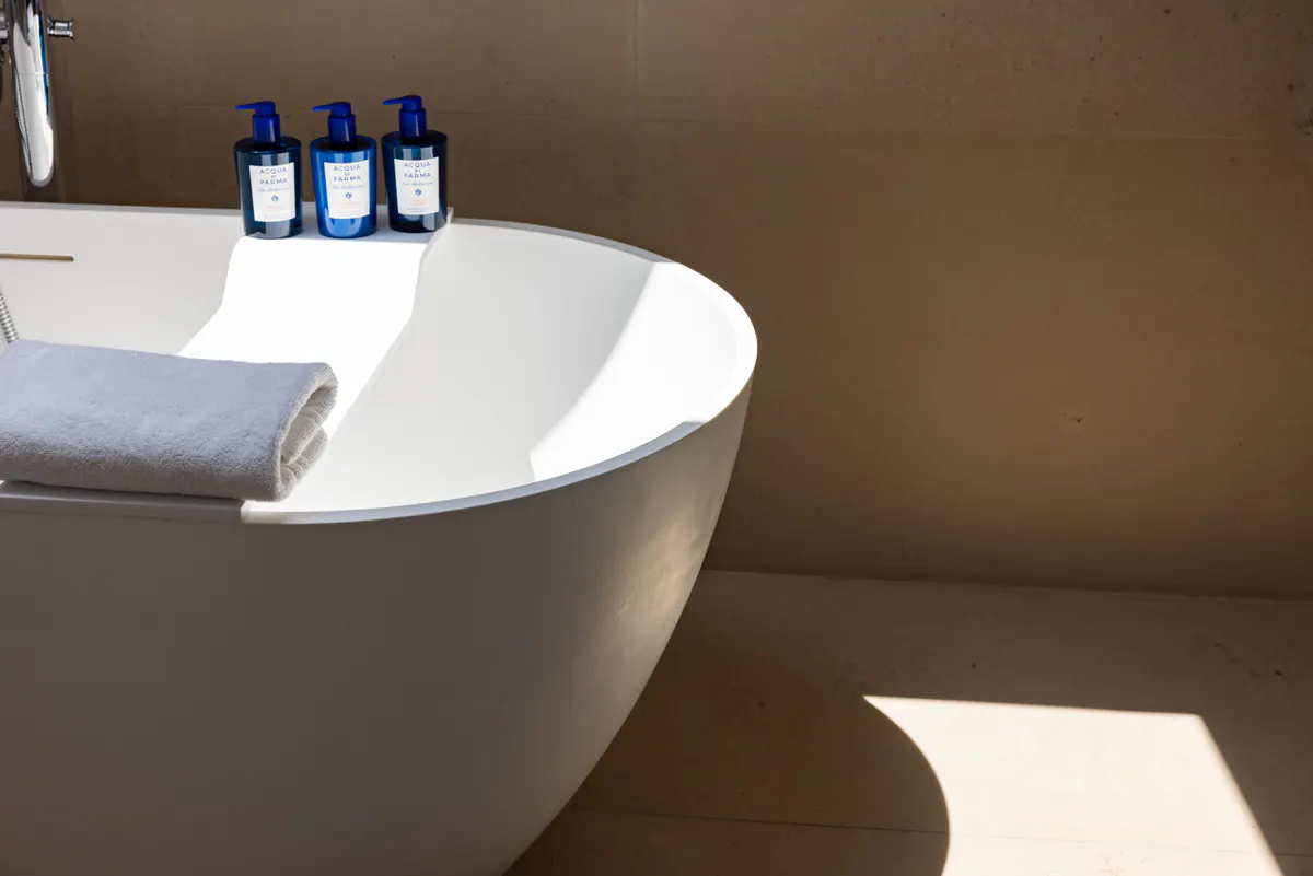 A white freestanding bathtub with blue accent bottles, minimalist bathroom in warm tones