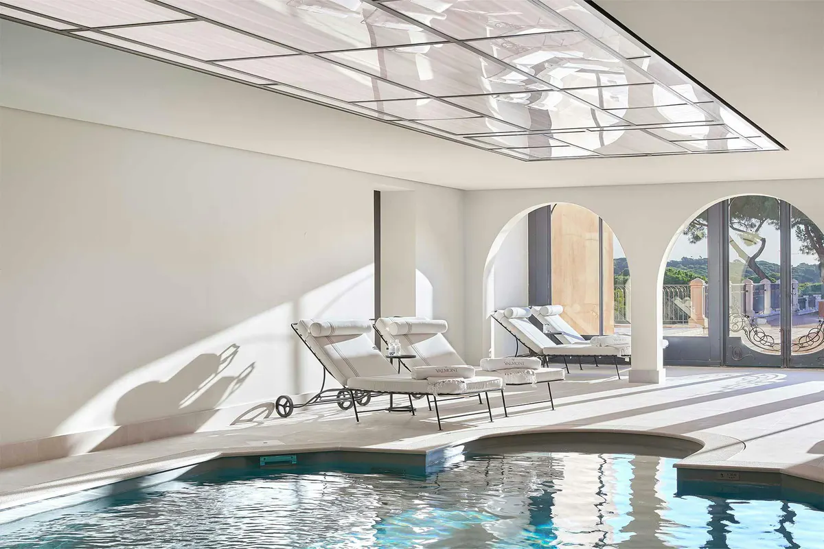 Indoor pool with skylights, white loungers, and bright natural illumination