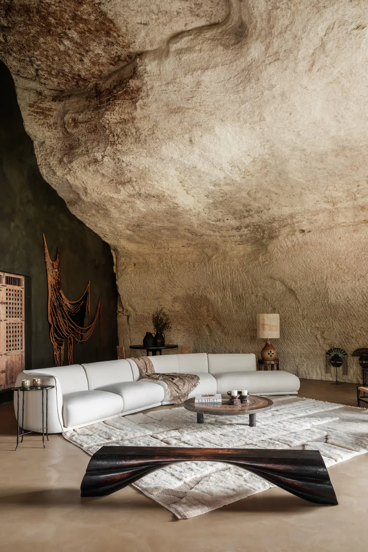 Cavernous living room carved into stone with monumental raw limestone wall, curved cream seating, arched opening