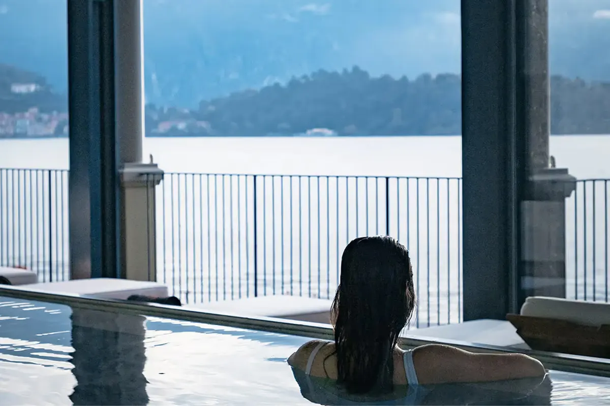 Person soaking in thermal spa pool with mountain-lake panorama