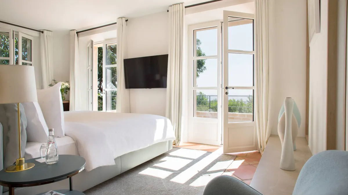 Bright bedroom with white bed and open doors to terraced seating