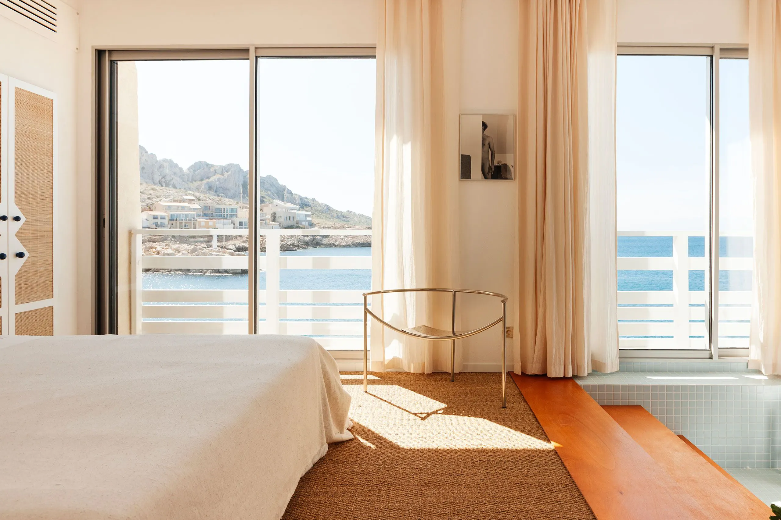 A cabanon bedroom at Tuba Club, its window open to the sea and the rocks of Les Goudes