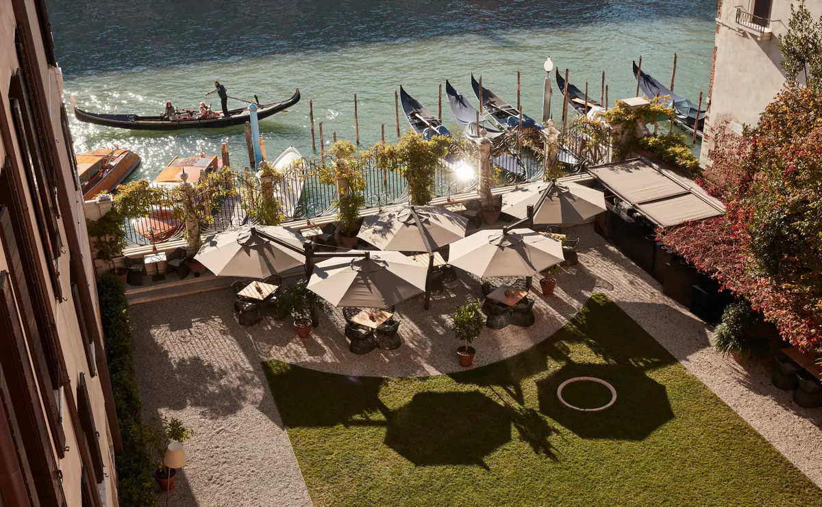 A waterside garden terrace with lounge seating and views of gondolas on the Grand Canal