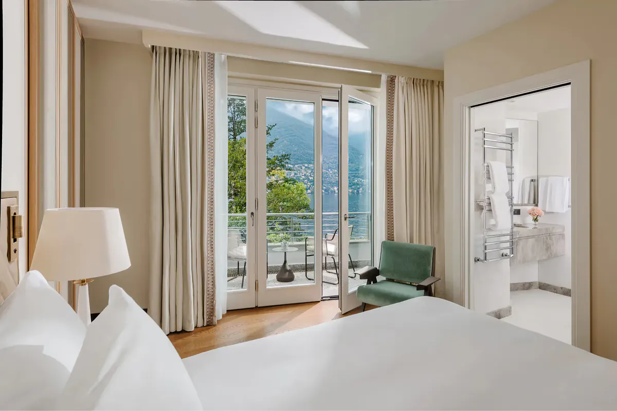 Guest suite with bed, cream furnishings, and balcony overlooking lake and peak