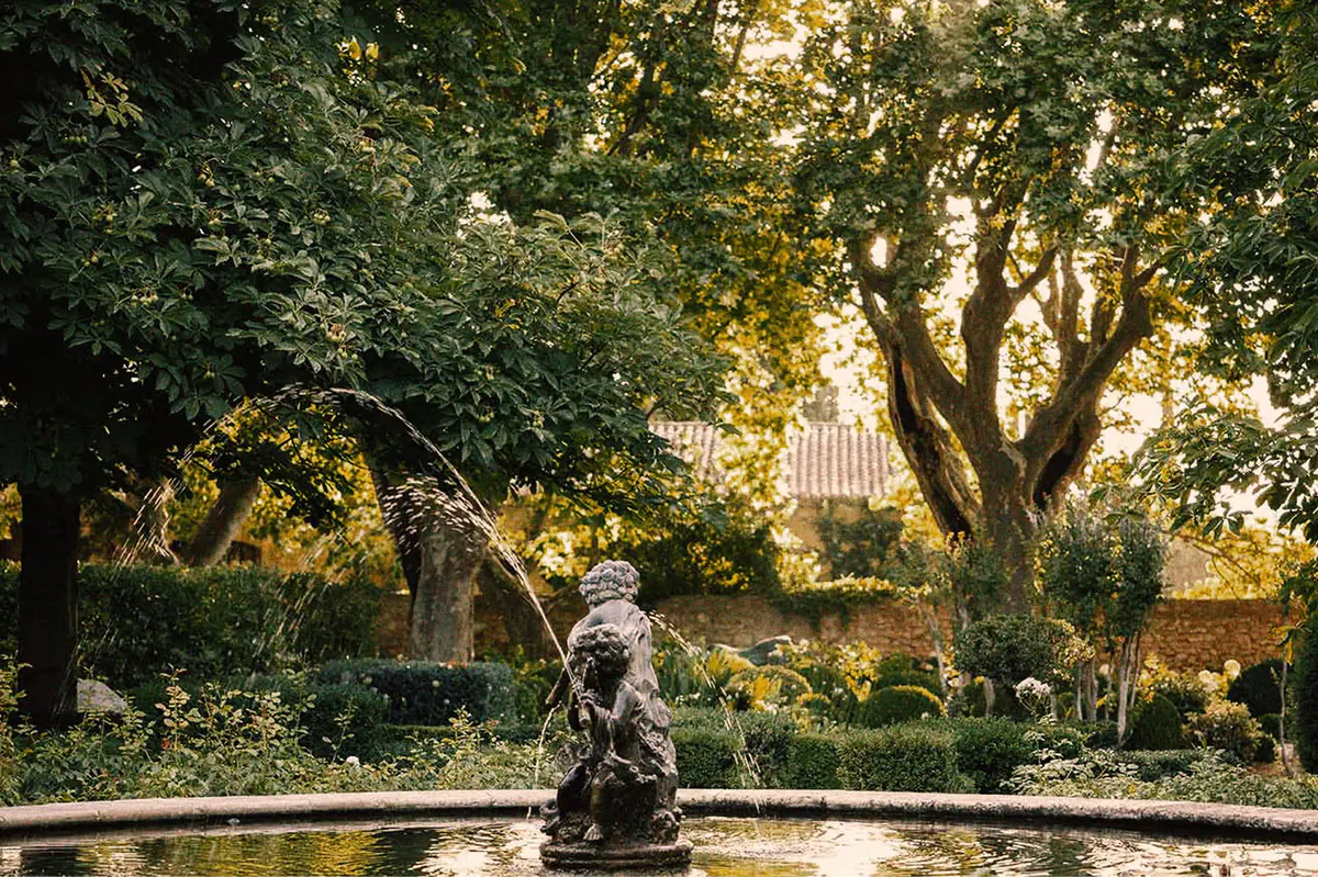 Fountain sculpture in garden courtyard surrounded by stone walls and mature trees