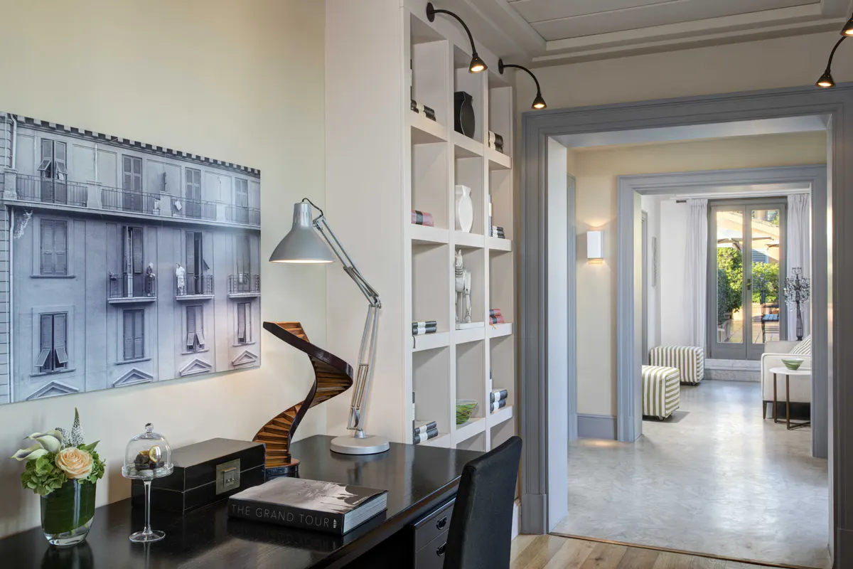 Writing desk with framed artwork, shelving, and doorway to adjoining room