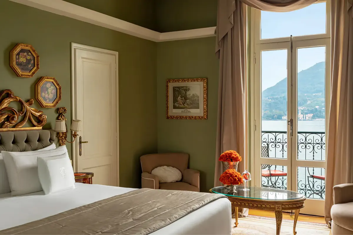 Bedroom with sage walls, white linens, and balcony doors to mountain lake views