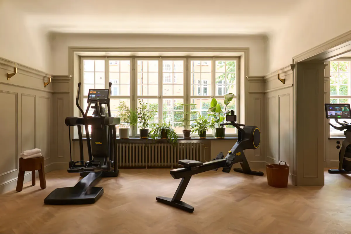 A fitness center with exercise equipment, large windows, and natural light from garden views