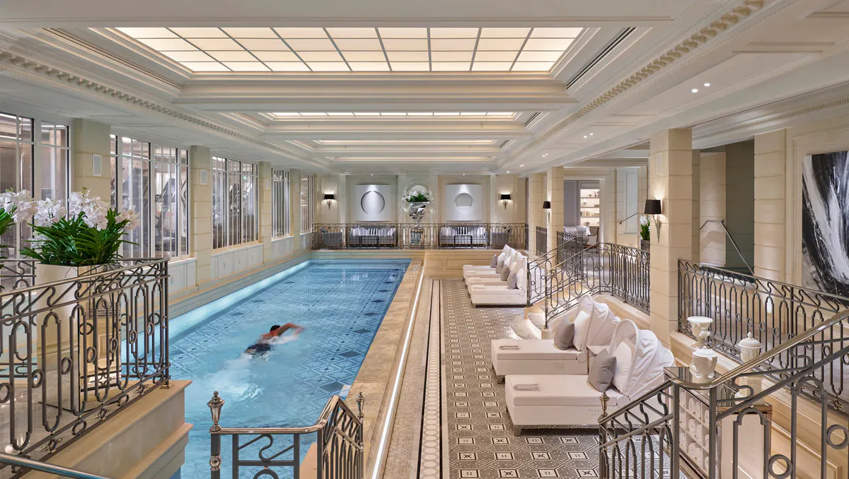 An indoor swimming pool surrounded by beige loungers and glass railings