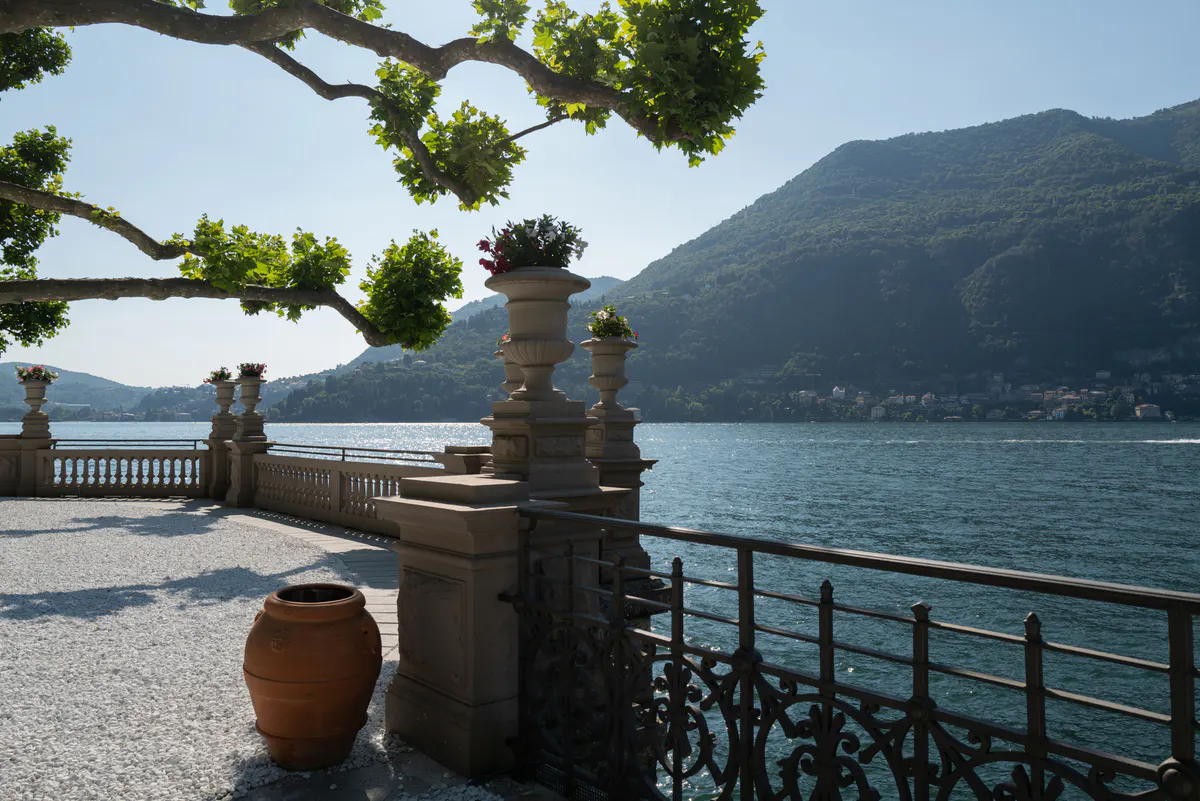 Lake vantage point framed by branches with stone balustrade, distant villages, and peaks