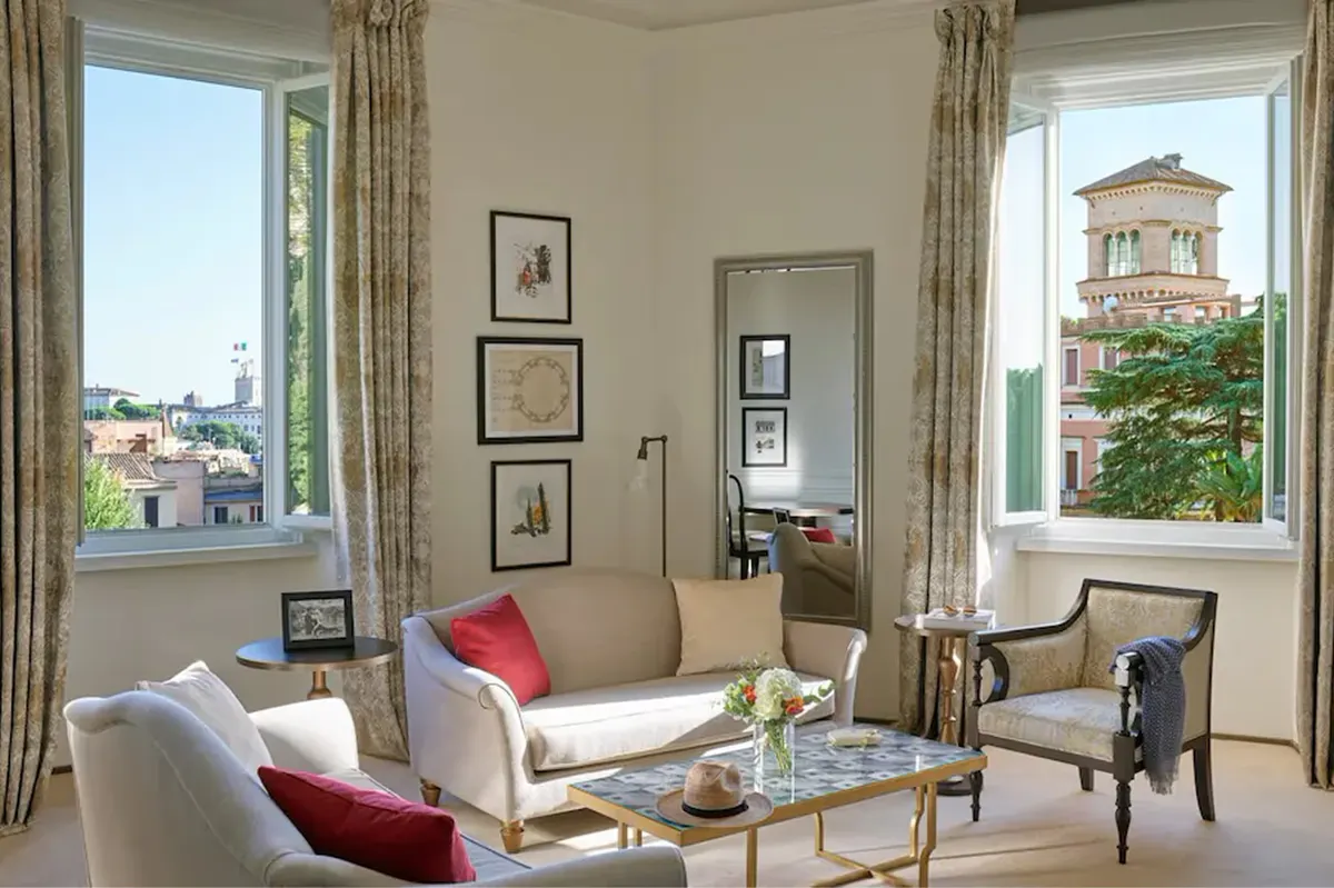 A sitting room with tall windows, beige furnishings, artwork, and panoramic views of Rome’s cityscape