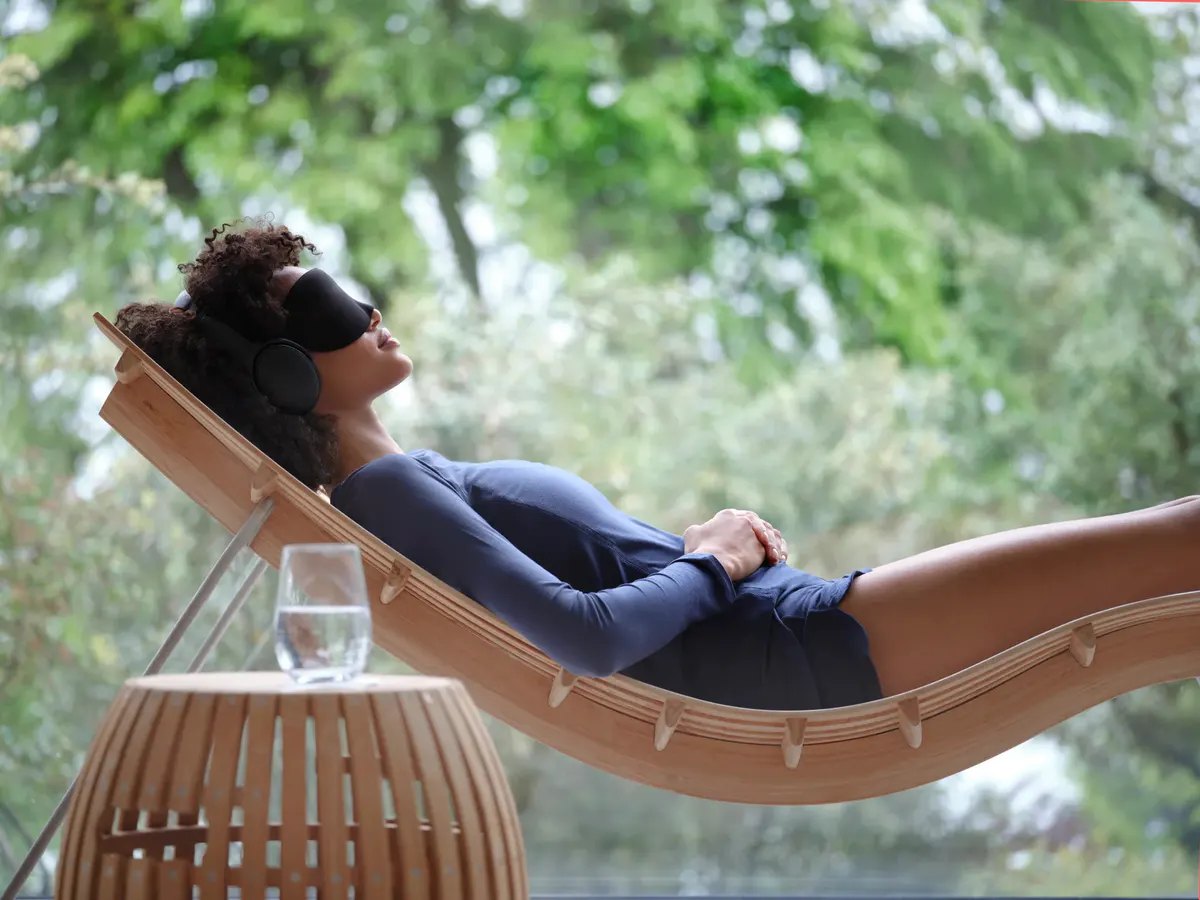Woman in black loungewear relaxing in wooden hammock suspended over green forest canopy