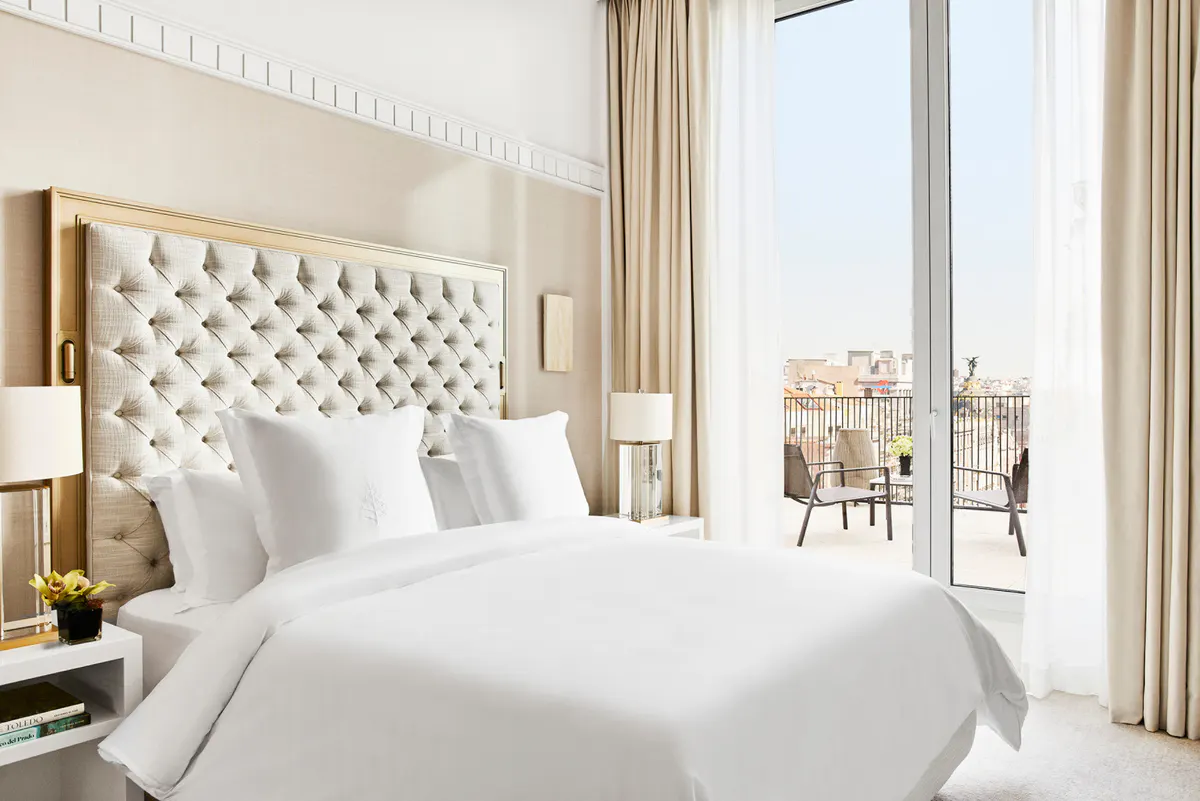 Bedroom with white quilted headboard, floor-to-ceiling windows, and balcony overlooking Madrid skyline