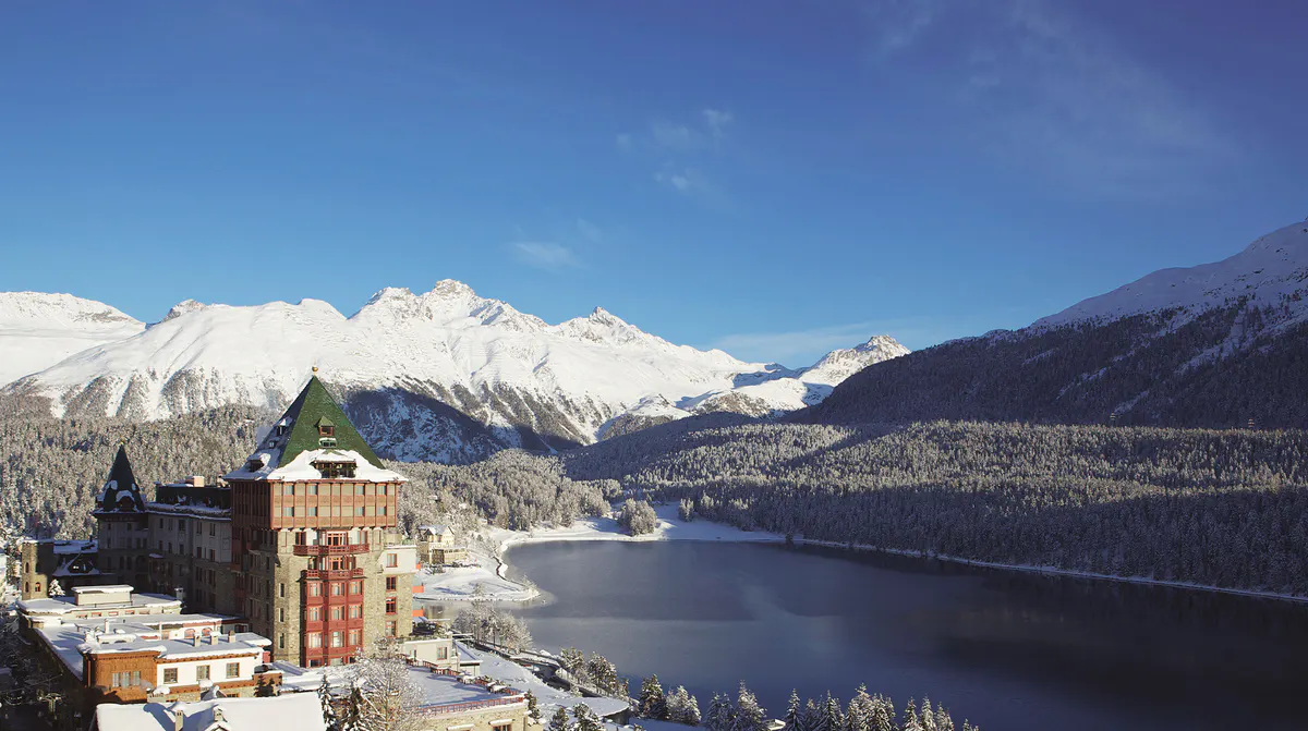 Exterior view of red-brick building on snowy lakeside with pine forest