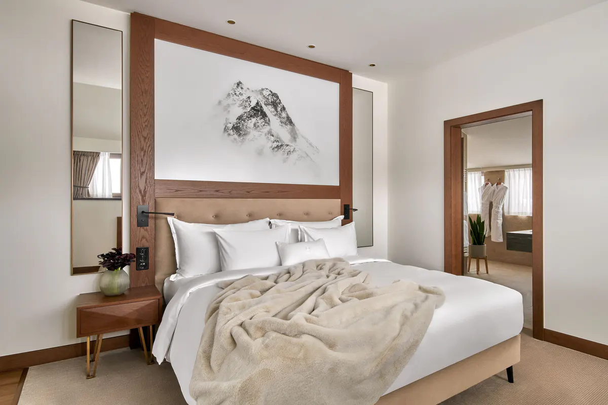 Bedroom with wood-framed headboard, gallery art, and neutral furnishings with mountain light
