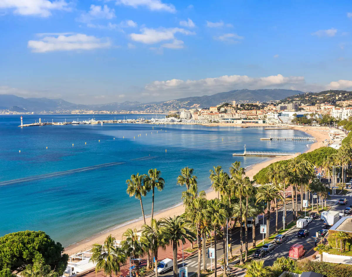 Coastal view of Cannes with blue waters, palm-lined Boulevard de la Croisette, and white sandy beaches