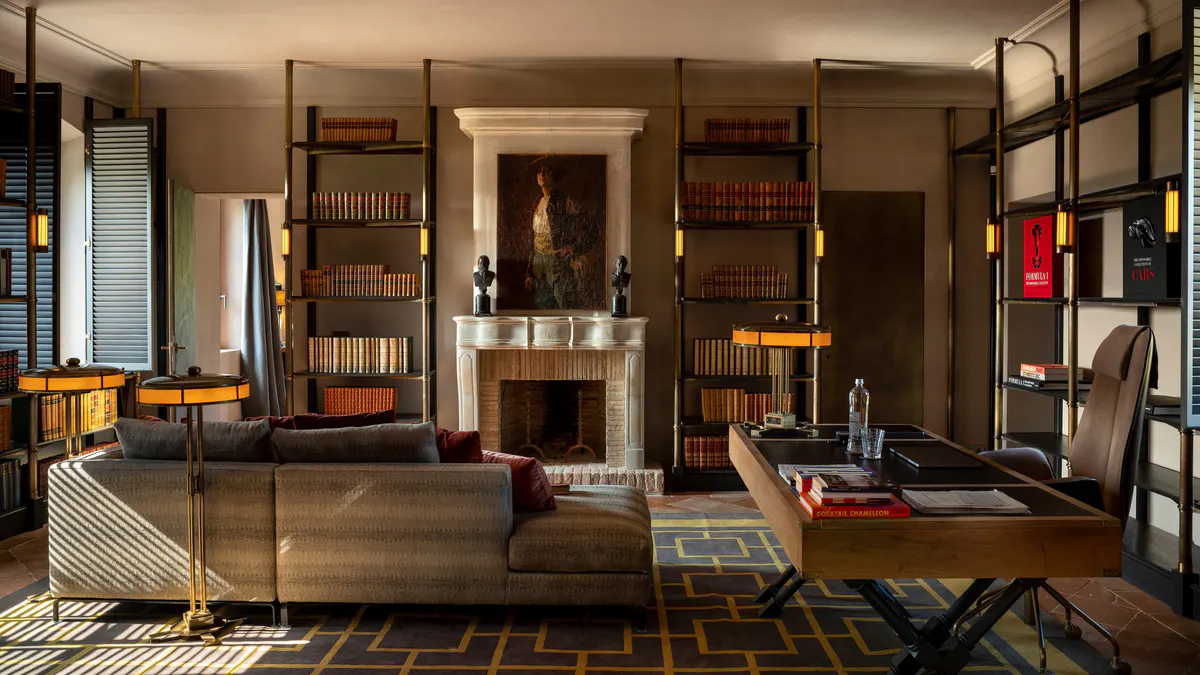 A library lounge with a stone fireplace, ladder shelving, and leather sofas around a brass legged table